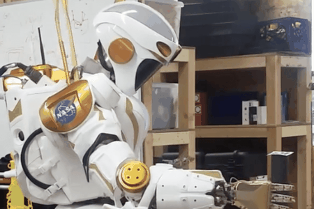 A NASA Valkyrie robot picks up an item with its hand.