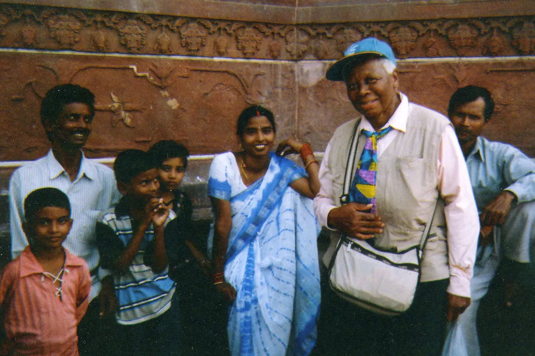 A woman wearing a baseball cap and colorful tie, stands with adults and children, smiling.