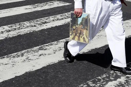 A fan carries a copy of ‘Abbey Road’ as he traverses the infamous crosswalk that appears on the album’s cover.