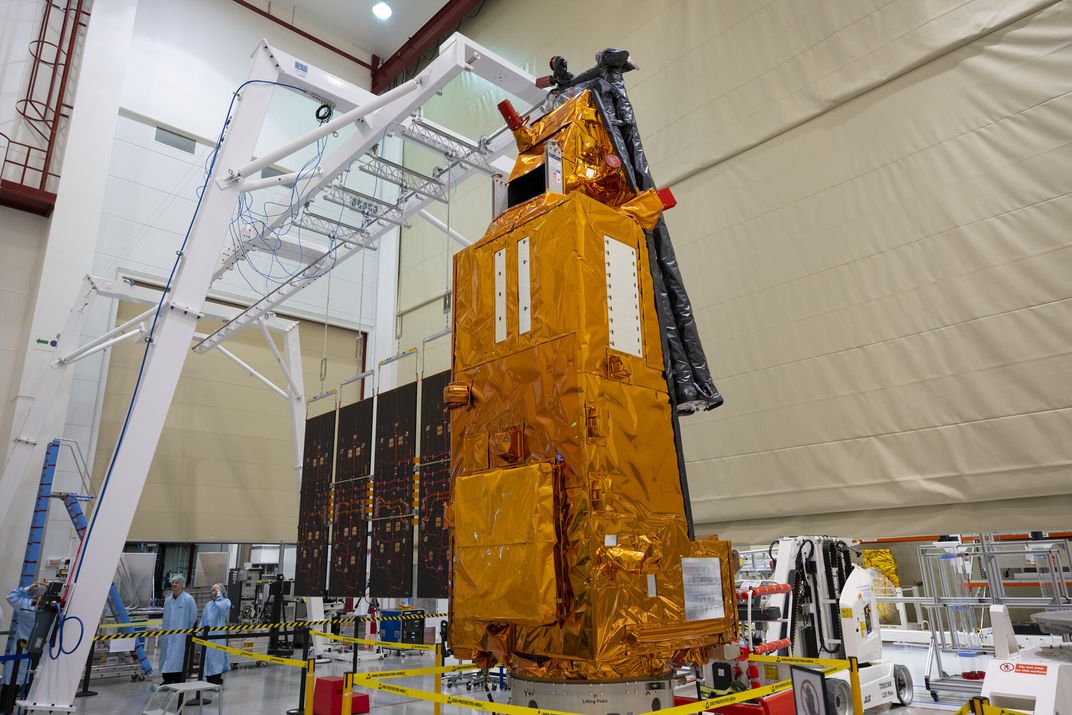 a tower-like object covered in orange foil sits in a cleanroom