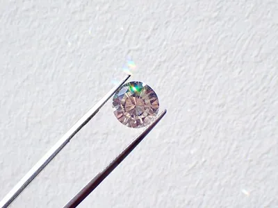 Silver tweezers hold a small diamond against a white background.
