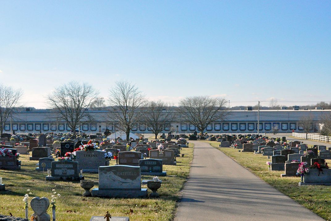 A photo of a modern cemetery shows two green plots split down the middle with a road.