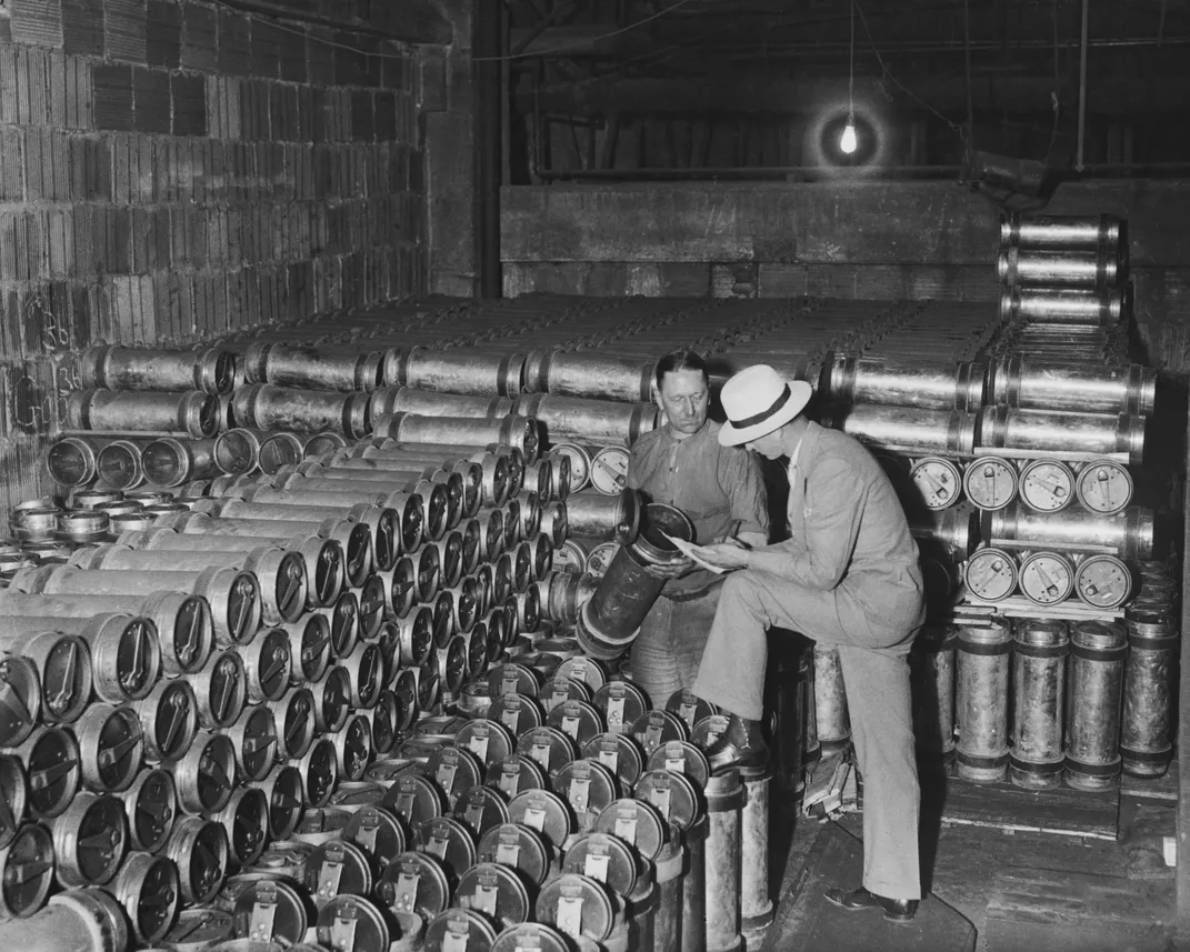 A circa 1915 photograph of two men standing next to 2,000 pneumatic tube carriers in the basement of a Post Office branch in Manhattan