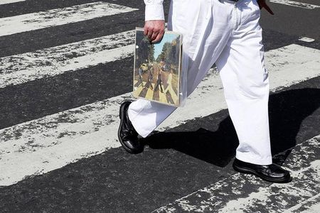 A fan carries a copy of ‘Abbey Road’ as he traverses the infamous crosswalk that appears on the album’s cover.