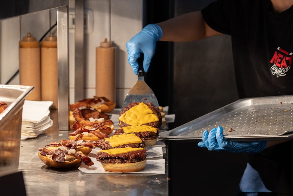 A person wearing gloves lifts burgers on to a tray