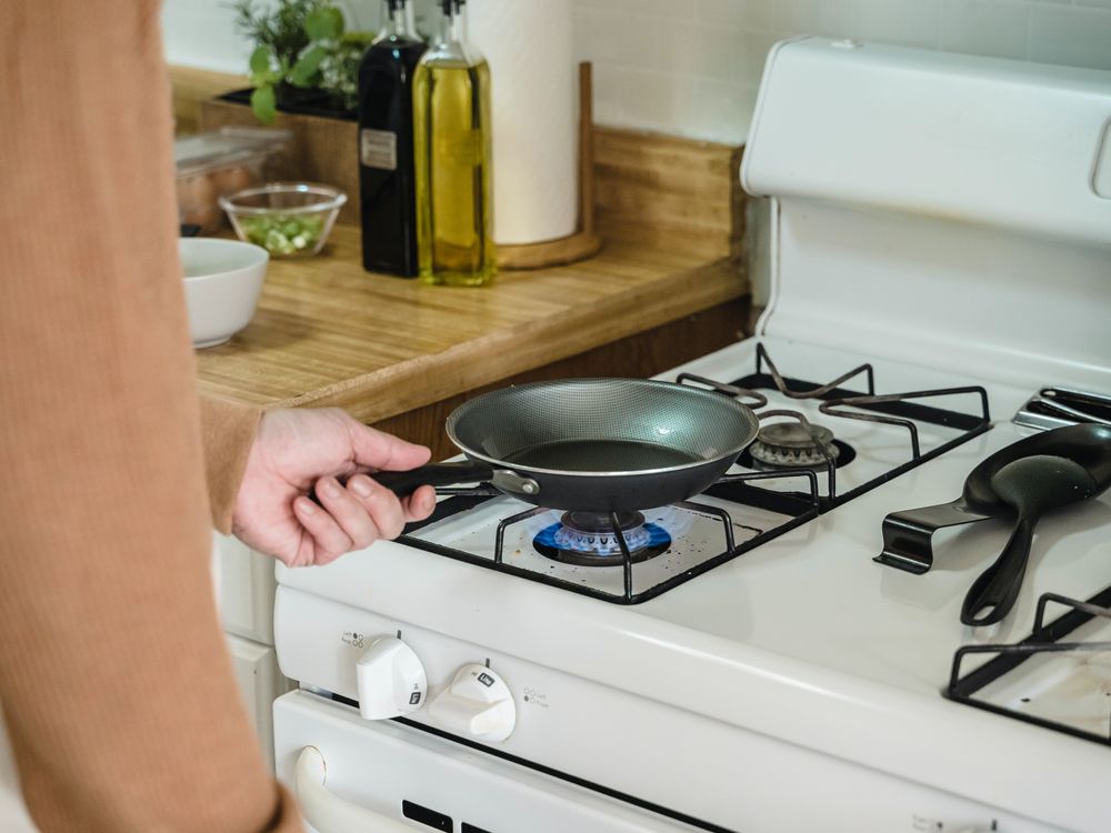 Person putting a frying pan on a white gas stove