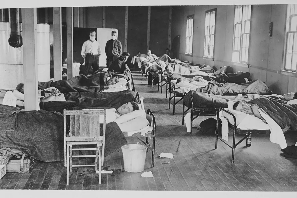 1918 flu patients lie in hospital beds, some turned to face the camera
