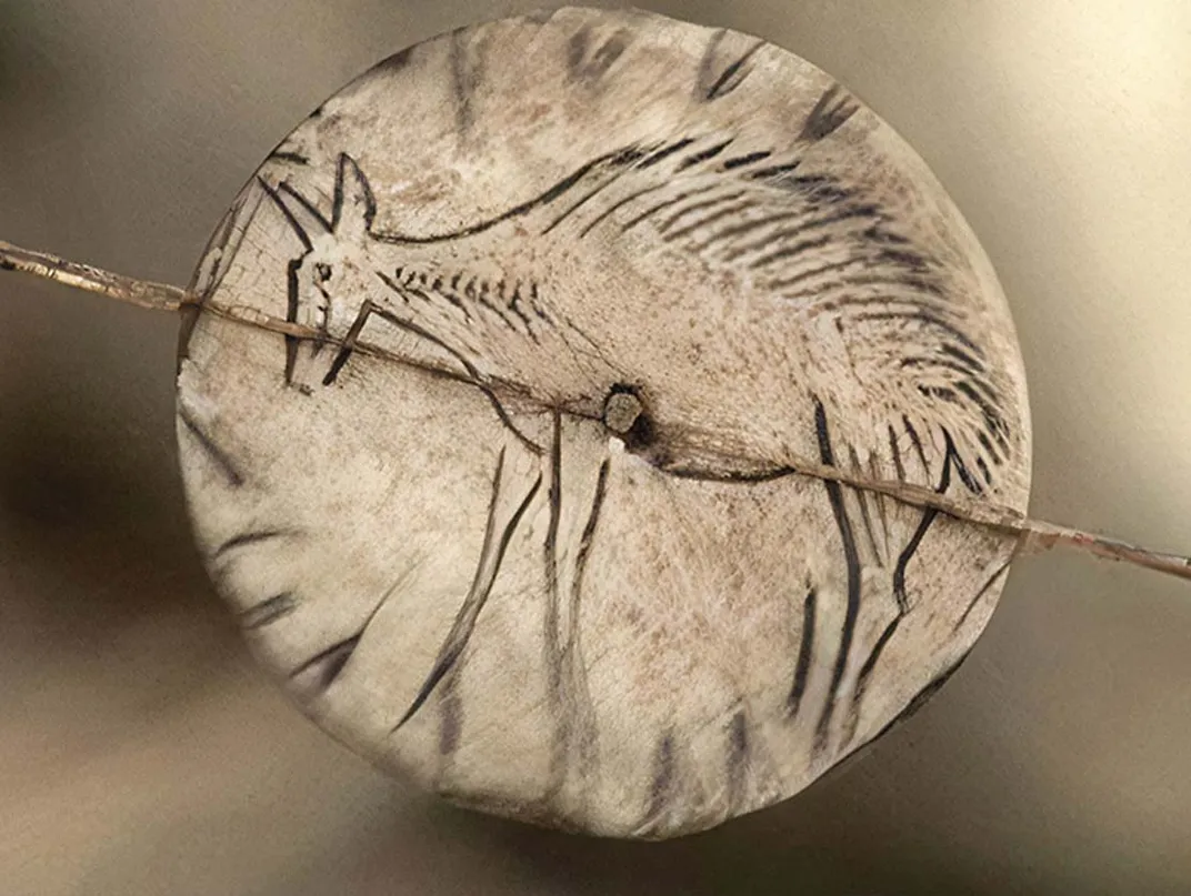 a small disk made of bone with animal etching spins on a string