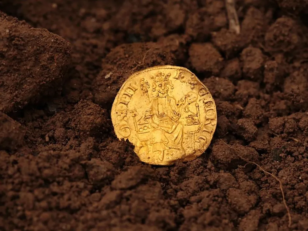 bright gold coin in dirt depicting crowned and bearded man