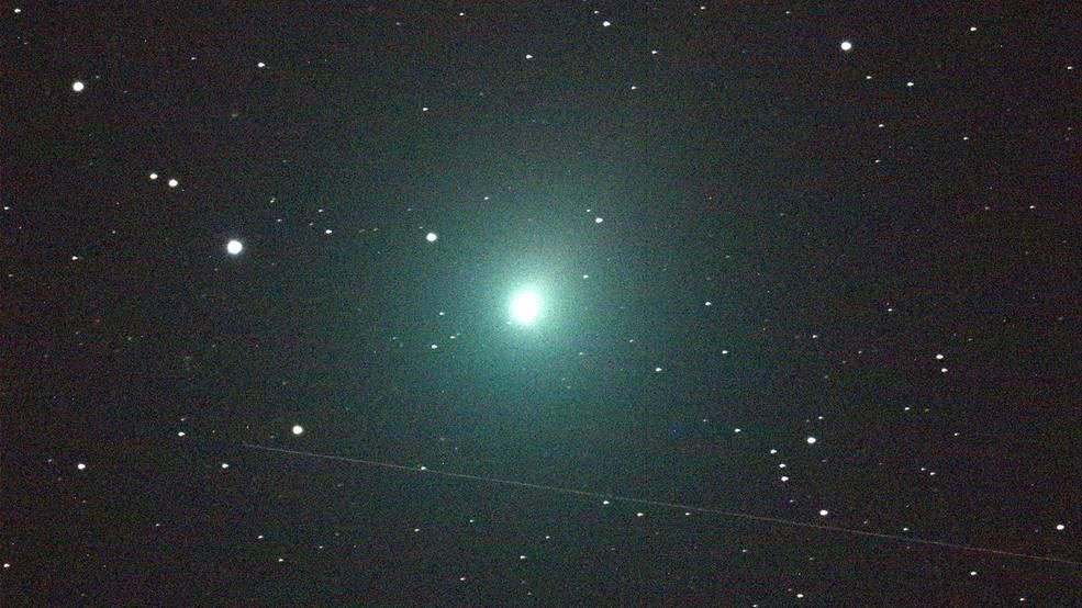 A photo of Comet 46P/Wirtanen. In the middle of the image is a ball of light that is glowing bright green against a starry black sky.