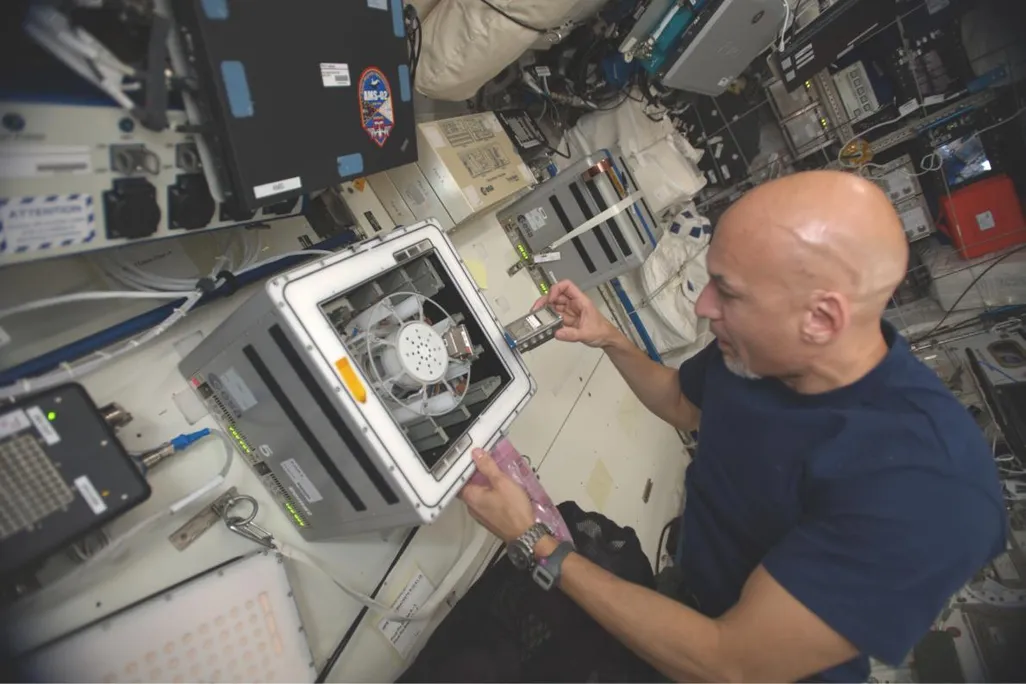 Astronaut in a blue t-shirt puts a small vial of bacteria and basalt in a centrifuge on the international space station