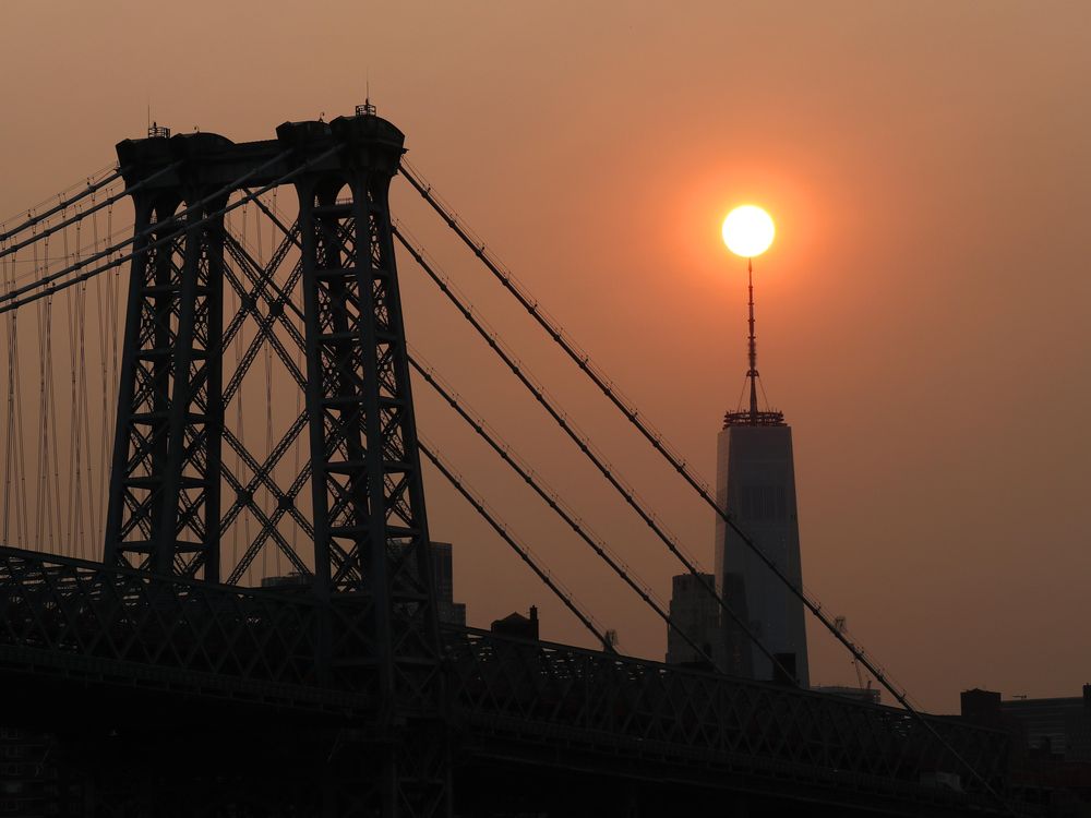 The sun sets behind the Manhattan Bridge and One World Trade Center in a haze created by smoke