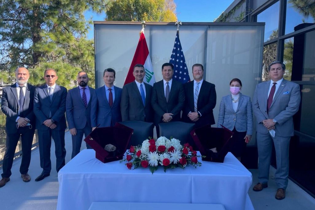 group of men and women in business attire standing outdoors in front of U.S and Iraq flags before two displays of stone tablet artifacts