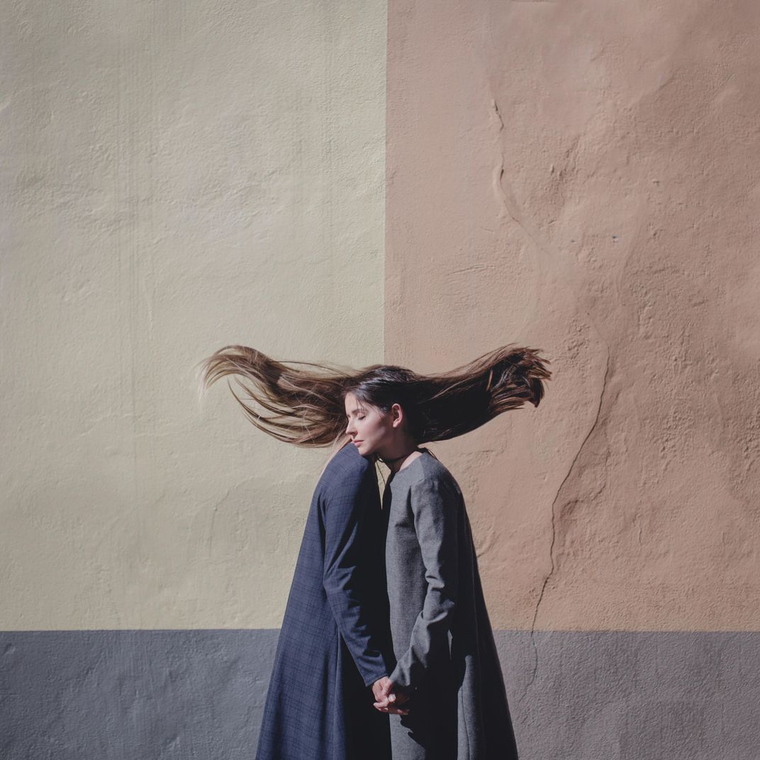 A surreal image with two women holding hands and leaning against each other, their hair suspended mid-air.