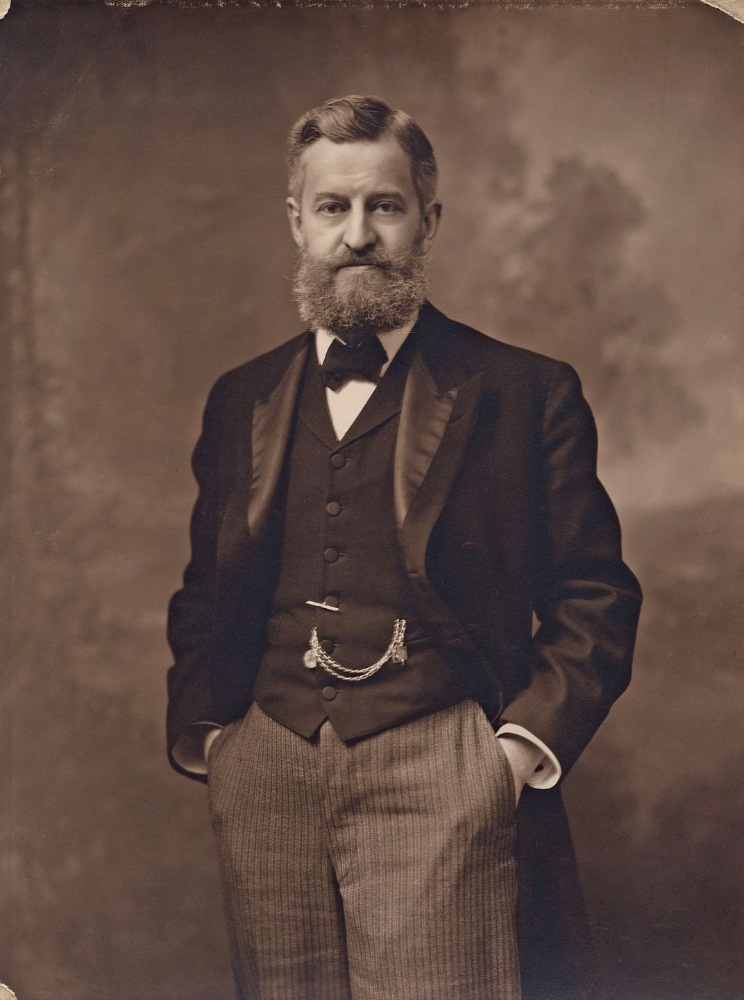 a black and white photograph of a bearded man in a suit standing for a portait