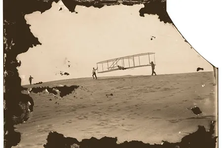 Day after day, the brothers (Wilbur, left, and Orville at the controls) put their new and improved glider through its paces. Assistant Dan Tate lent a hand.