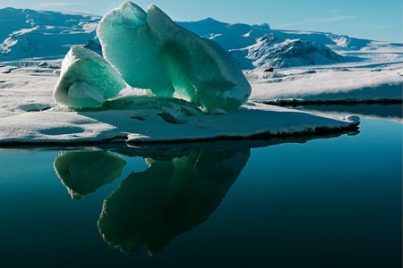 Lake Jökulsárlón shimmers with the reflection of a magnificent iceberg. This lake, located at the edge of Vatnajökull, Iceland’s largest ice cap, formed slowly when part of the glacier began to recede in the 1920s. The glacier continues to calve (split), releasing more icebergs into the expanding lake. 