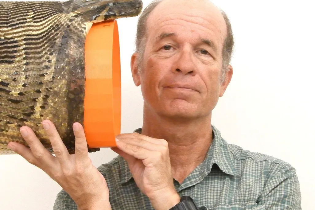 A man holds a snake head with an orange bucket-like object in the mouth