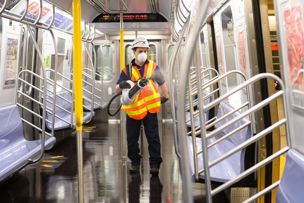 MTA worker wearing hard hat, mask, and safety vest uses a bulk disinfectant machine to deep clean an MTA subway car