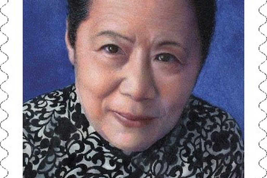 A postage stamp picturing a close up of nuclear physicist Chien-Shiung Wu. She has dark hair is wearing a black and white patterned dress.  Chien-Shiung is pictured against a dark blue background 