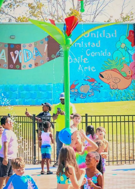 Kids play under a playground water fountain, with the mural in the background.
