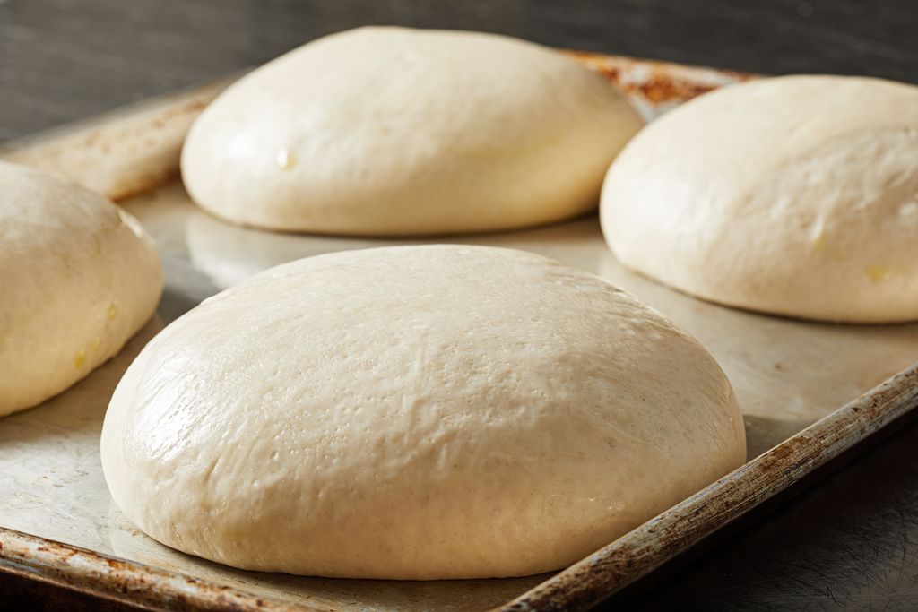 Four balls of pizza dough rising on a baking sheet