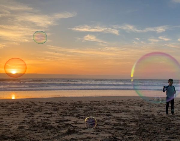 A boy blows bubbles at the beach at sunset thumbnail