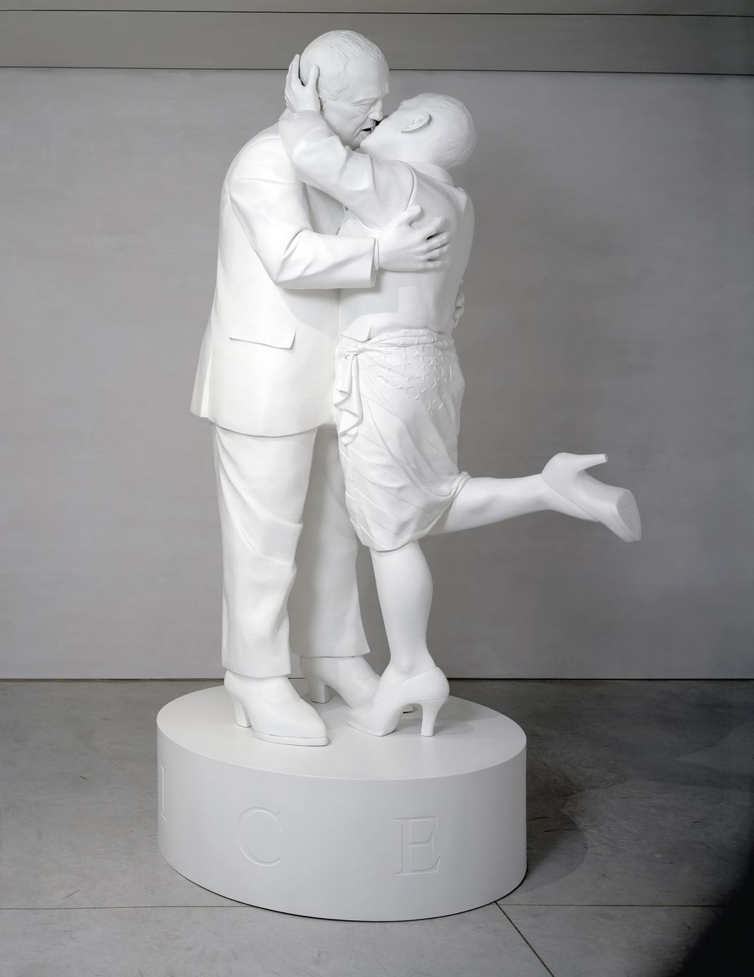 A white statue, in neoclassical fashion, of two men in high heels and suits kissing