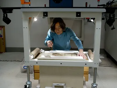 Conservator Jiro Ueda positions the handscroll prior to reflectance imaging spectroscopy. A large camera mounted above his head captures images through a hole in the table