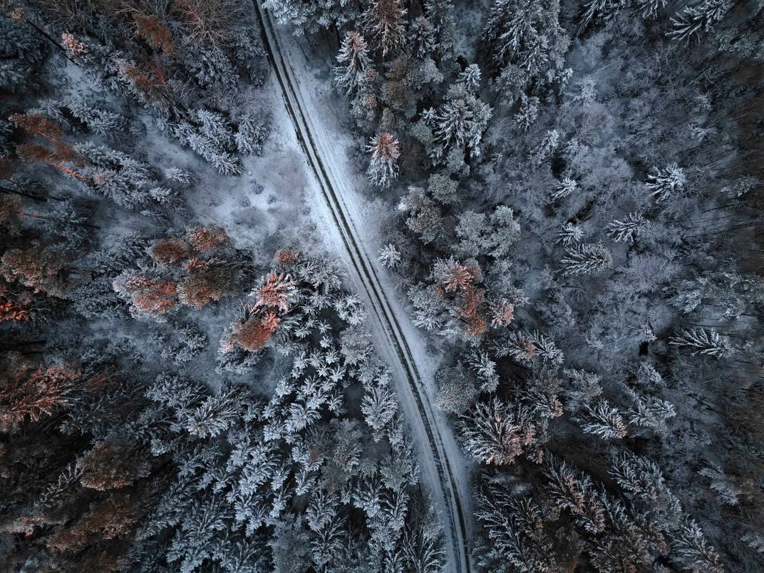 a snow-covered road in a forest is shown from above