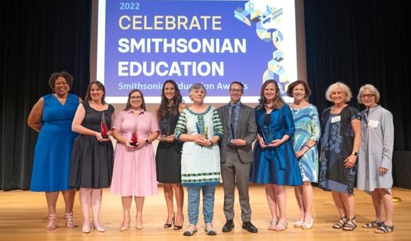 A group of people posing for a photo on a stage.  Dr. Monique M. Chism with Awardees and Smithsonian Women’s Committee supporters at the 2022 Smithsonian Education Awards Ceremony, July 28, 2022.