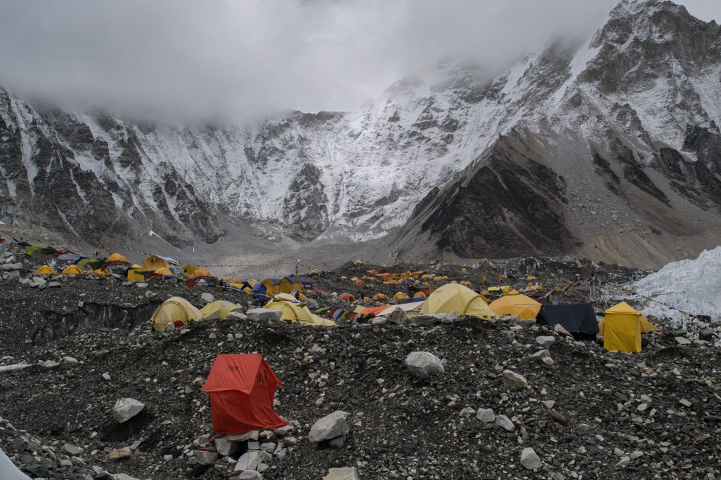 yellow and orange tents dot a rocky mountainside with peaks in the background obscured by storm clouds