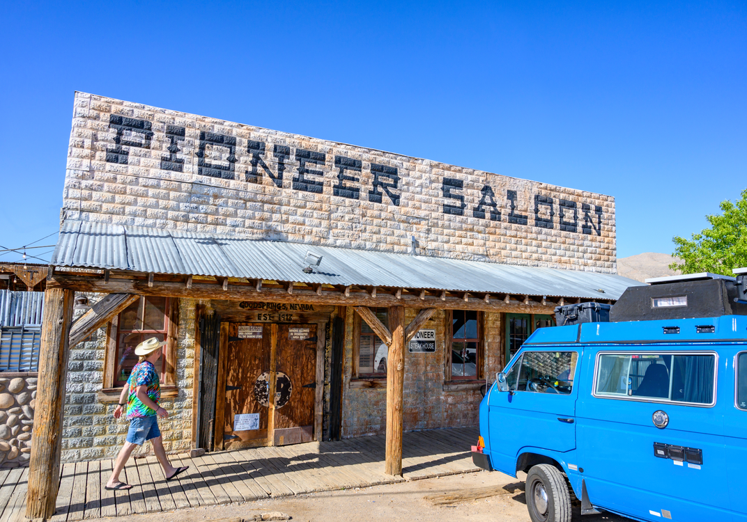 A person walks past the Pioneer Saloon building with a blue van parked nearby.