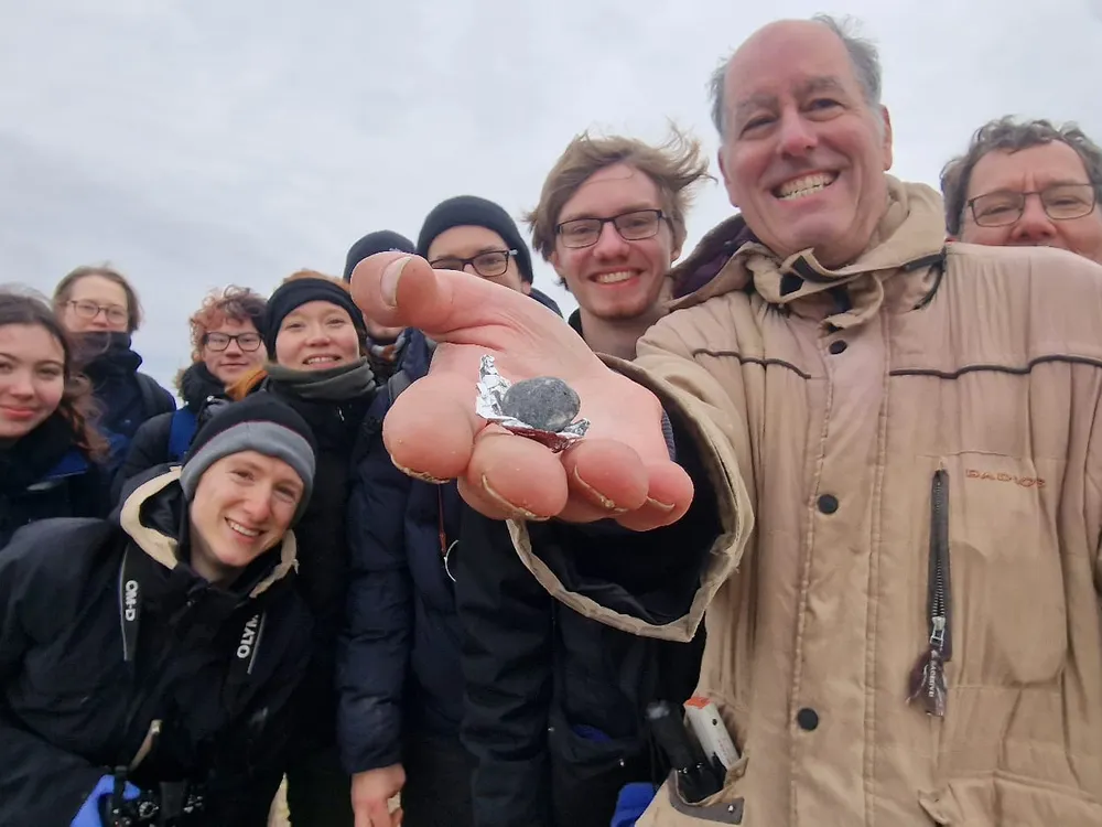 about ten people smiling with one holding a very small rock