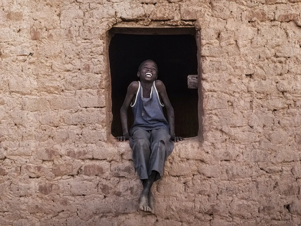 A teenage young African boy sits in a empty windowsill