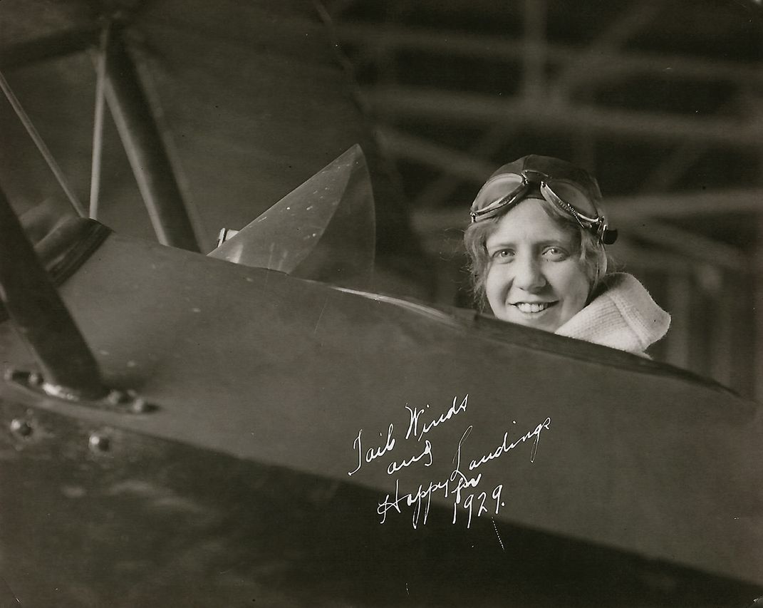 An autographed black and white photograph of a woman wearing flight goggles sitting in the cockpit of an airplane