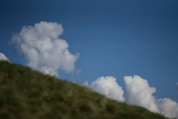 Clouds blooming over a grassy hill thumbnail