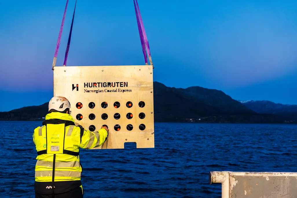man wearing safety gear touches crate filled with wine hanging from crane