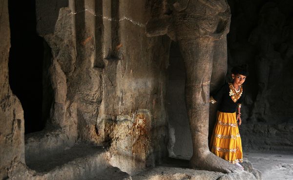 A young girl peers out from between the stone feet of Shiva - Elephanta Caves, near Mumbai, India thumbnail