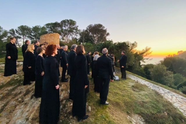 Several people dressed in all black stand together on a hilltop with a sunset or sunrise in the background.