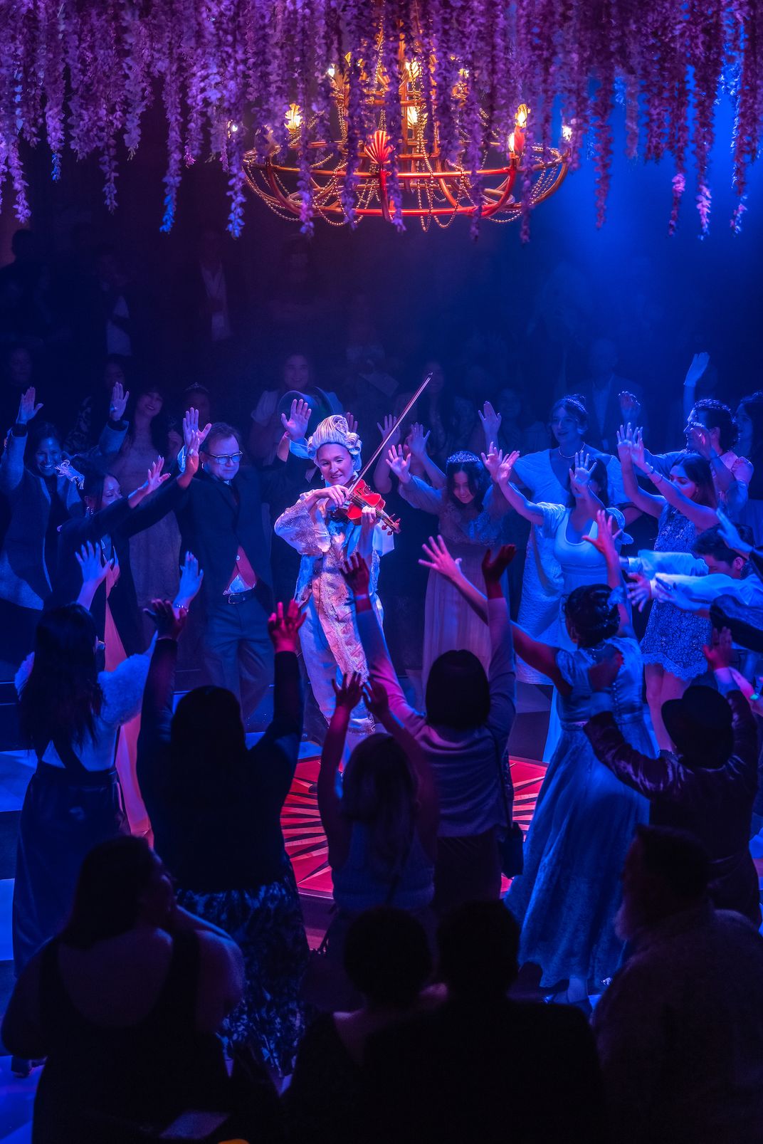 a violinist in a wig plays as people raise arms toward her