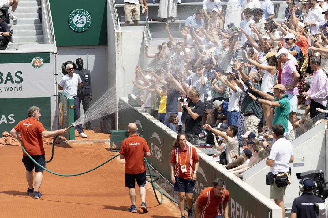 an official sprays a crowd of tennis spectators with a hose on a hot day
