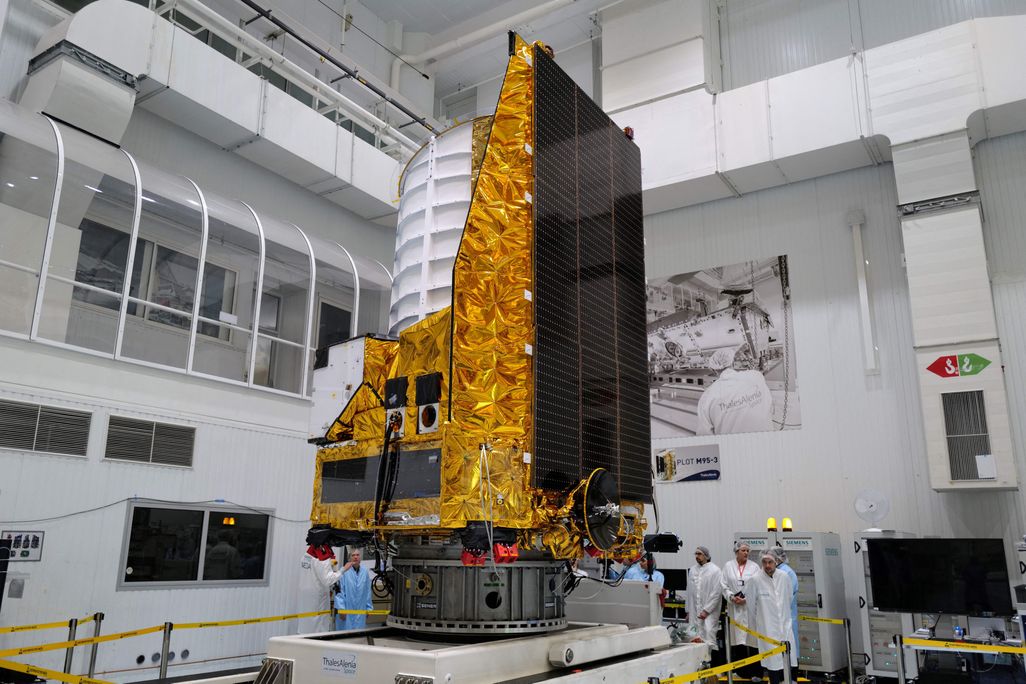 The gold and white Euclid telescope sits in a lab with scientists observing it.