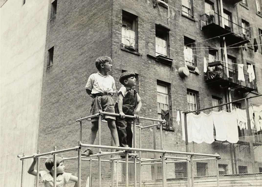 a black and white photograph of children playing on a jungle gym in a city setting
