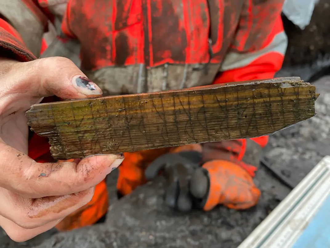 A closer view of the wet wooden slat bearing Norse runes