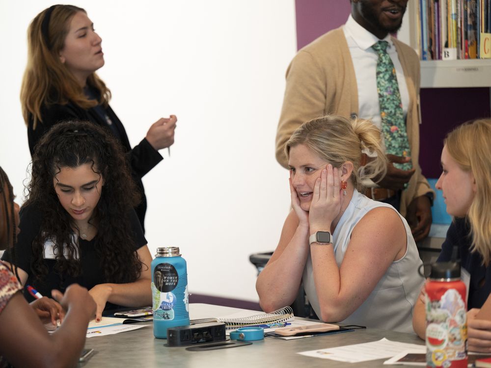 Teachers converse at a table, one woman with blond hair has her hands to her face