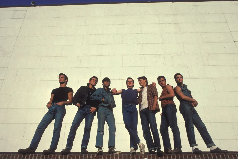 The cast of The Outsiders pose in front of a brick wall