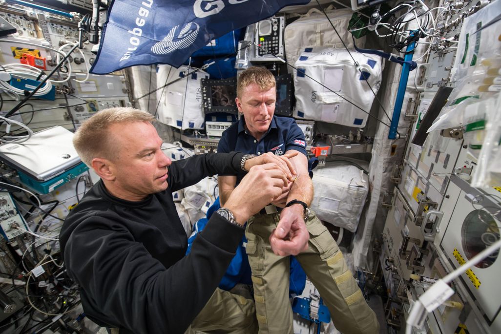 A male NASA astronaut Tim Kopra performs blood draw on European Space Agency astronaut Tim Peake on the international space station