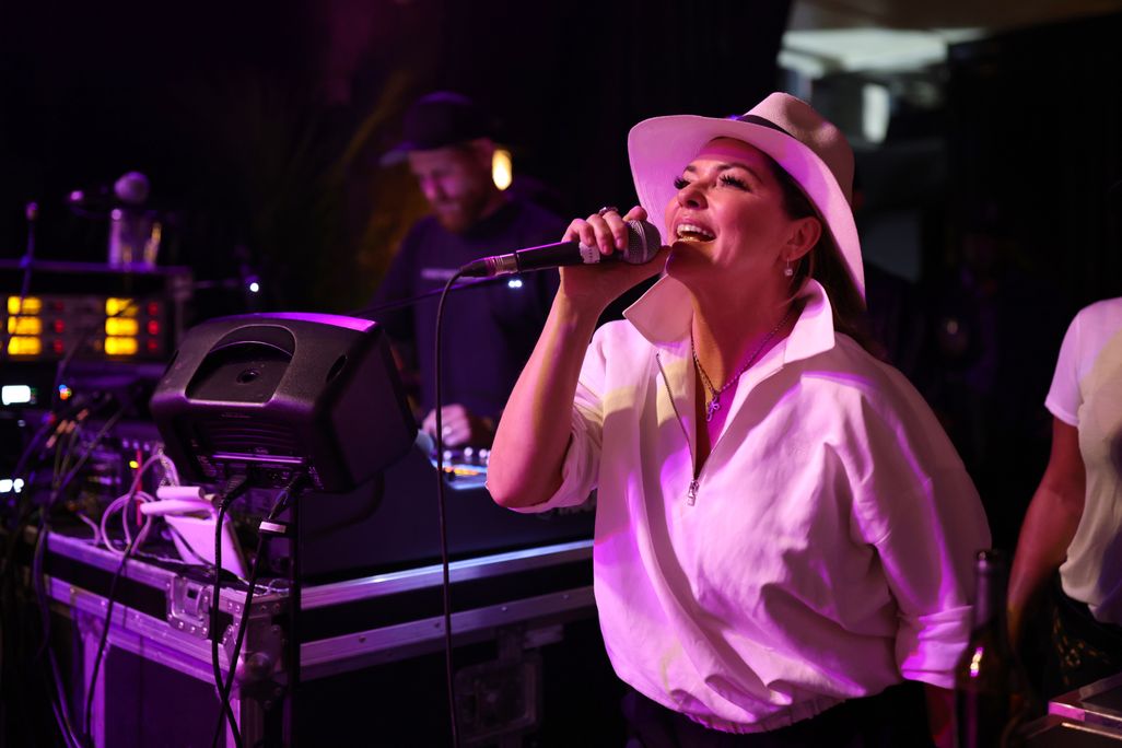 Shania Twain in a white shirt and hat singing on stage