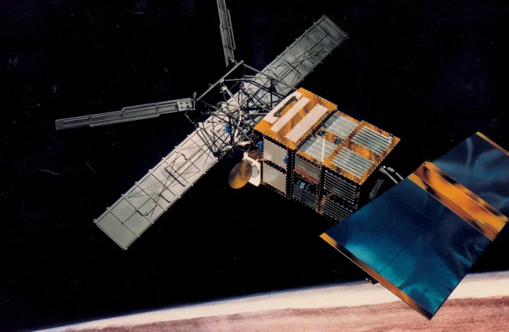 An illustration of the ERS-2 satellite floating in space; orange and blue rectangle instruments on the right resemble solar panels, while a 'K' shaped grey panels extend on the left. An orange and gray box sits in the middle, connecting these two parts.